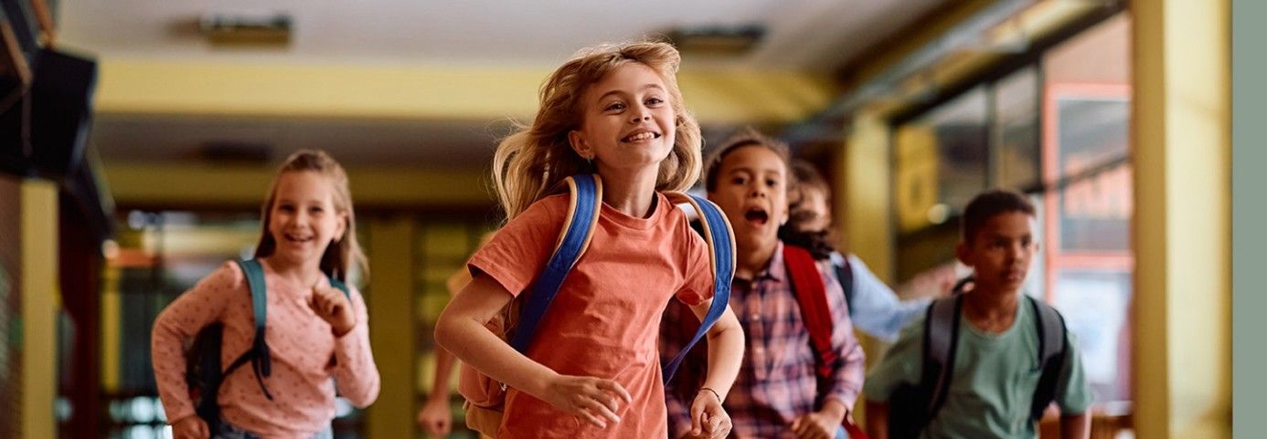 Grupa zadowolonych dzieci biegnie z plecakami przez szkolny korytarz.
