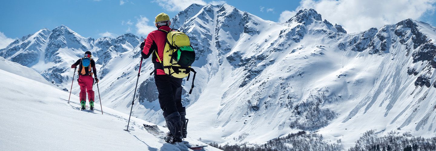 Dwie osoby z plecakami wspinają się w nartach zimą