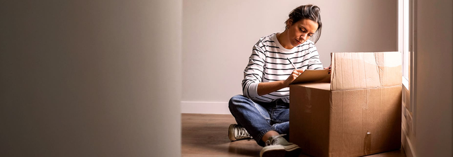 Kobieta siedząca na podłodze i opisująca karton przeprowadzkowy