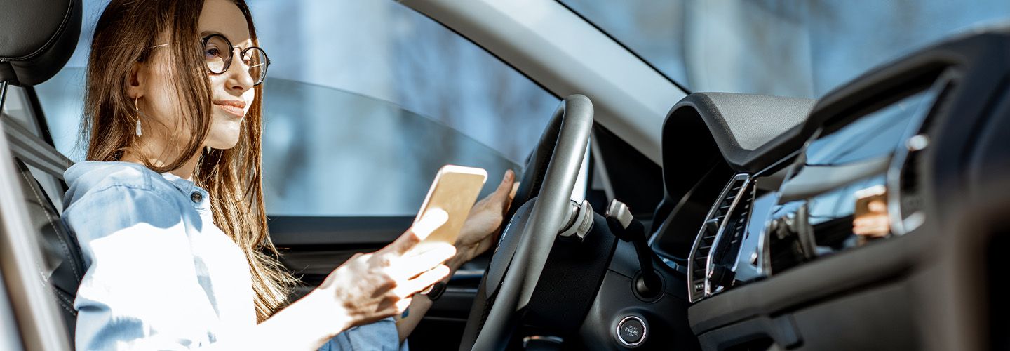 Kobieta sprawdza ubezpieczenie OC w swoim telefonie siedząc za kierownicą samochodu