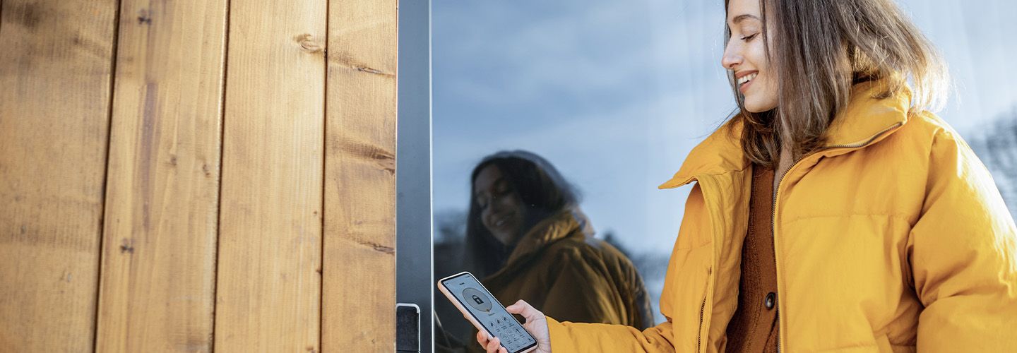 Kobieta sprawdza zabezpieczenia za pomocą smartfona stojąc przed drzwiami domu