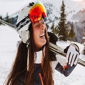 Narciarka z nartami na ramieniu smieje się stojac na stoku