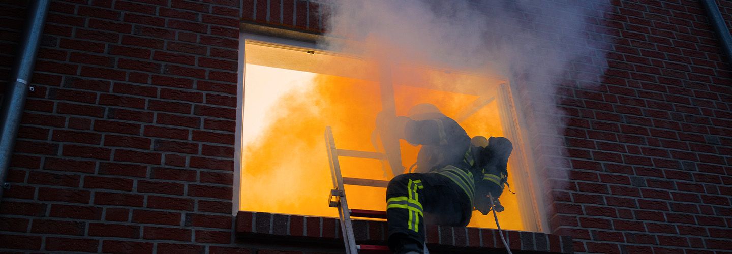 Strażak na drabinie gasi pożar przez okno budynku