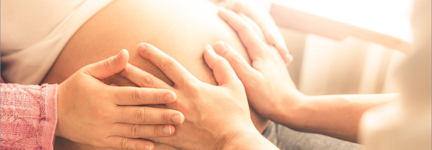 Dłonie mężczyzny i kobiety oczekujących narodzin dziecka obejmują ciążowy brzuch przyszłej mamy