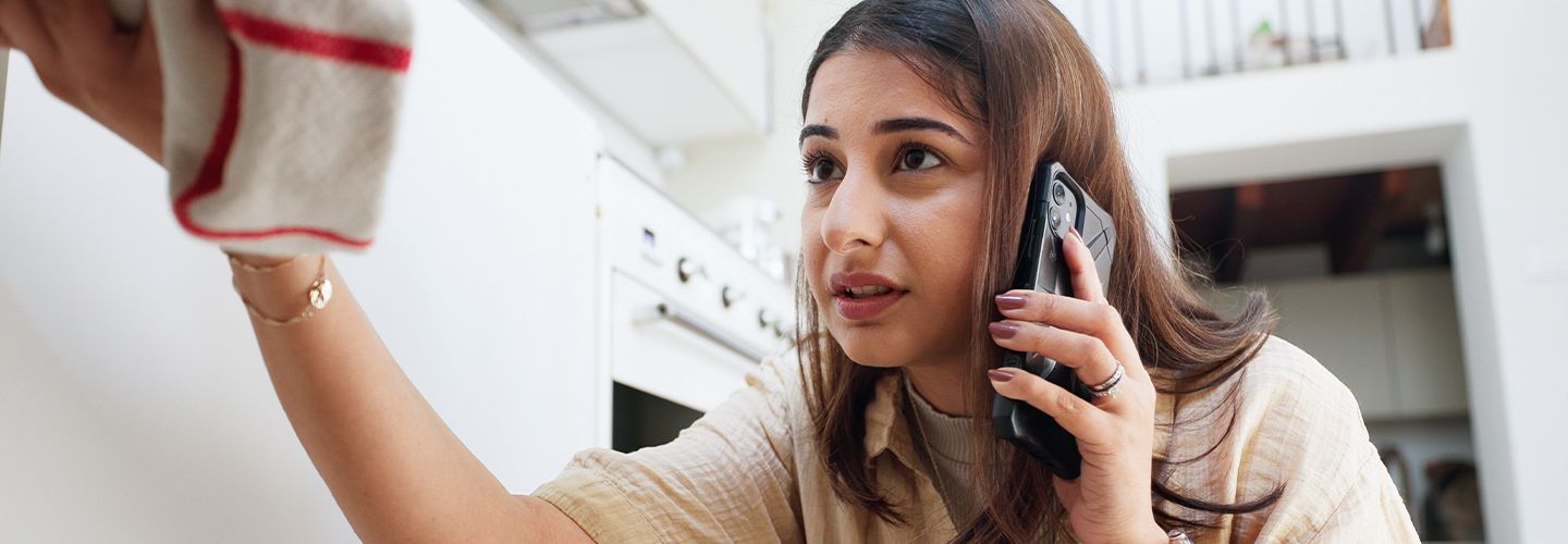 kobieta wzywa przez telefon pomoc do cieknącej rury próbując jednocześnie zbierać wodę ścierką - tytułowa.