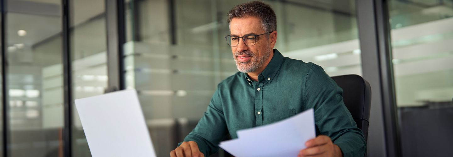 Mężczyzna przegląda dokumenty korzystając z laptopa.