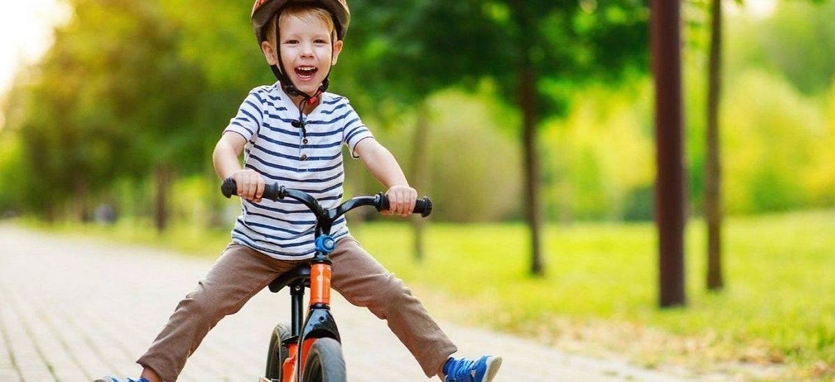 mały chłopiec w kasku jedzie na rowerku biegowym z nogami rozstawionymi na boki