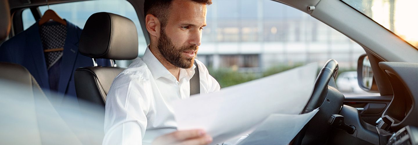 mężczyzna przegląda dokumenty siedząc za kierownicą swojego samochodu