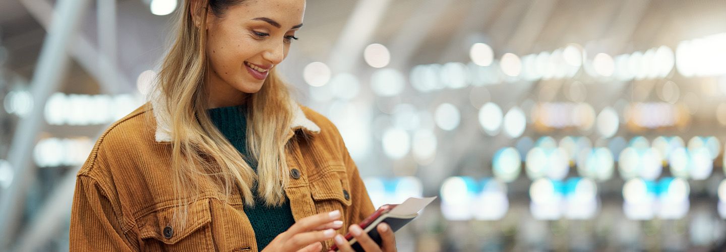 młoda kobieta stojąc na lotnisku dopełnia przez Internet formalności związanych z podróżą za granicę