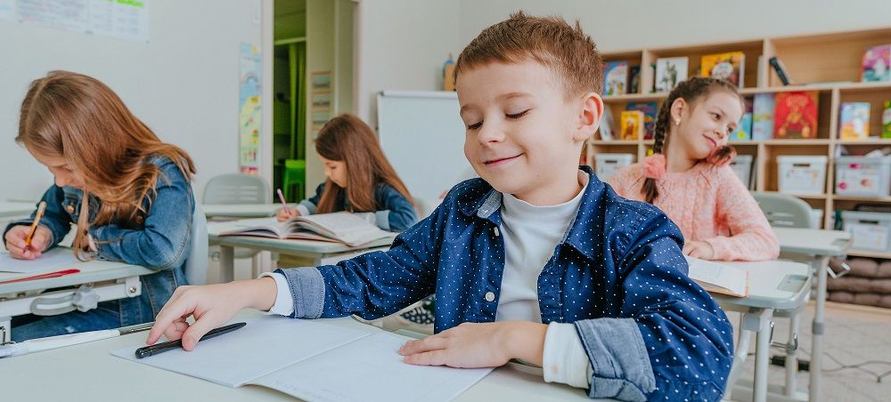 Dzieci siedzą przy ławkach podczas zajęć w klasie.