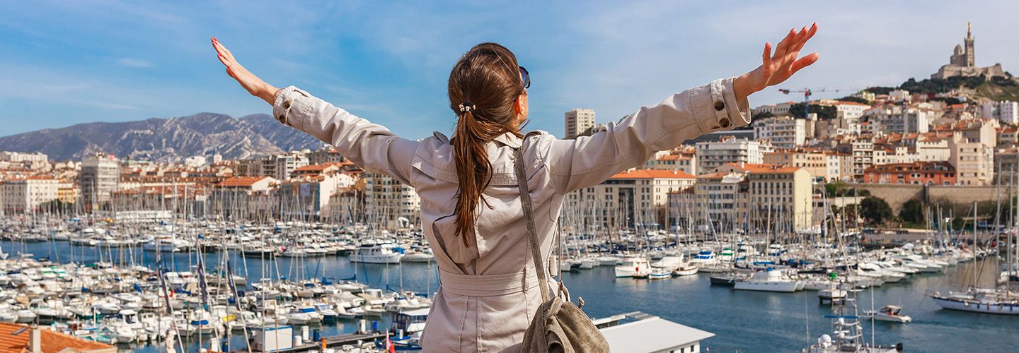 szczęśliwa turystka w czasie wakacji za granicą stoi na tle portowego miasta z rękami uniesionymi do góry