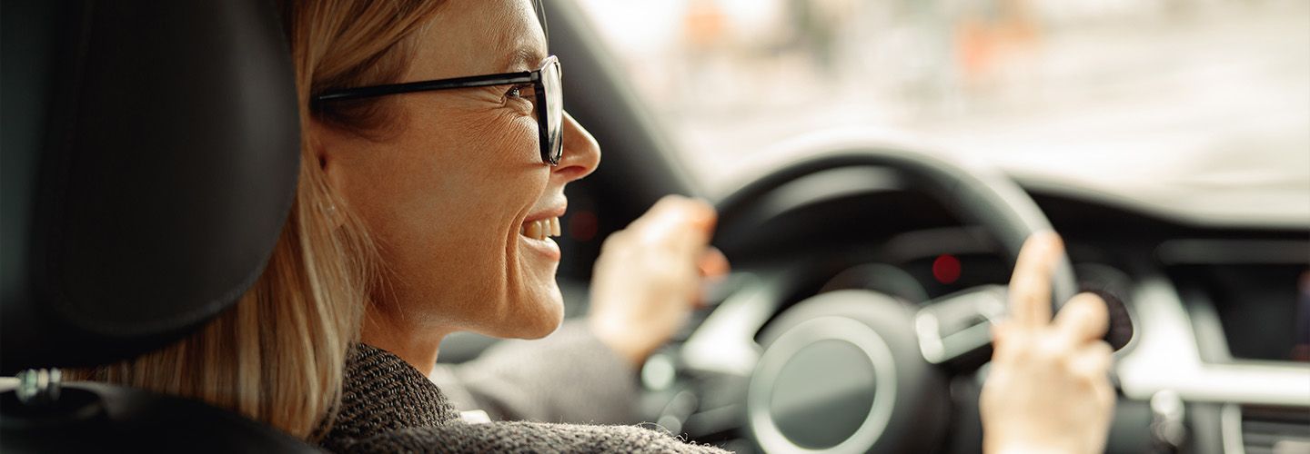 uśmiechnięta kobieta siedzi za kierownicą samochodu